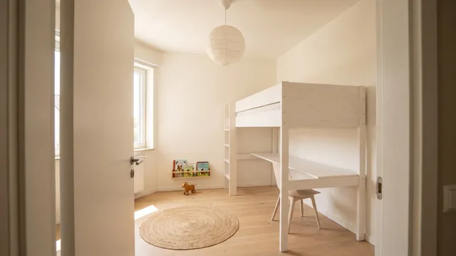 Symbolbild (KI-generiert): kleines Kinderzimmer mit weißem Hochbett, darunter Schreibtisch und Regal, Tageslicht vom Fenster