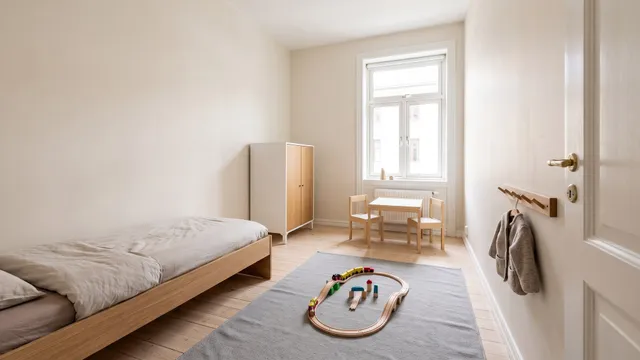 Symbolbild (KI-generiert): kleines Kinderzimmer mit Bodenbett an der Wand, kleinem Schrank, Kindertisch am Fenster, grauem Teppich und Wandgarderobe neben der Tür