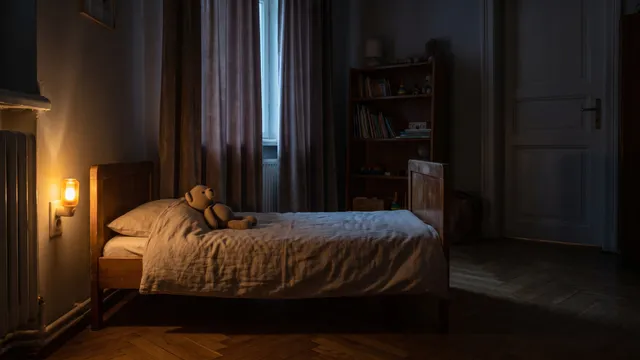 Symbolbild (KI-generiert): dunkles Kinderzimmer, ein warmes Steckdosen-Nachtlicht neben einem niedrigen Holzbett